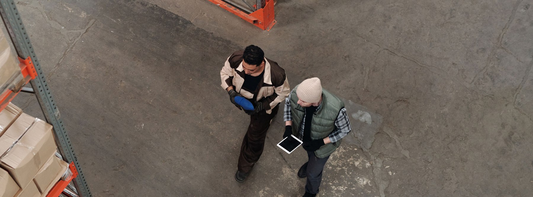 Two warehouse professionals reviewing operational information on a tablet from above.